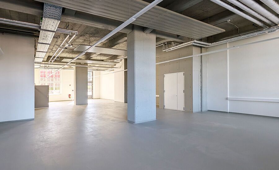 Leere Werkstatt mit viel Tageslicht, in deren Mitte eine große Säule als architektonisches Highlight steht