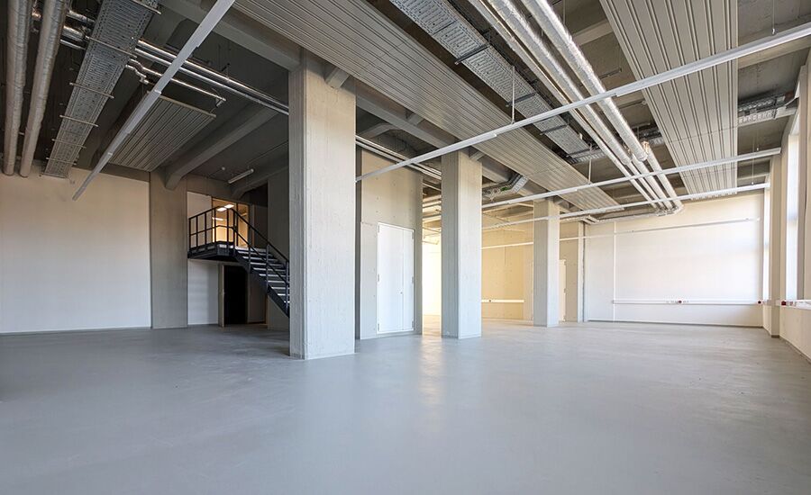 Leere, helle Werkstatt mit mehreren großen Säulen und einer Treppe, die verschiedene Ebenen miteinander verbindet